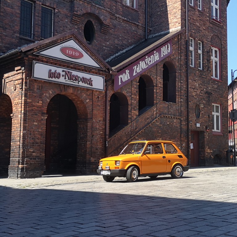 żółty fiat 126p na tle murowanej kamienicy